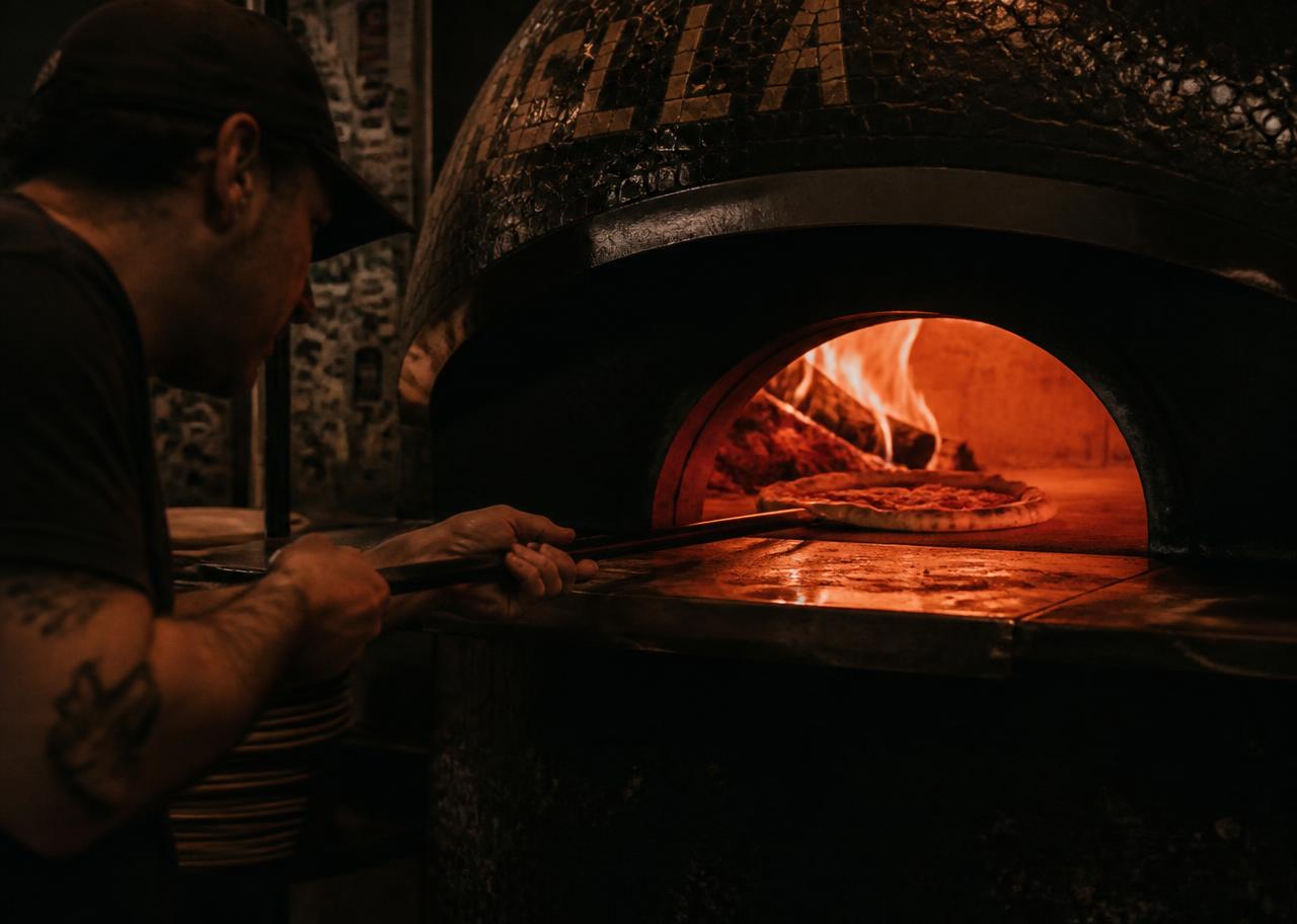 Pizzaiolo schiebt eine Pizza in den Holzofen